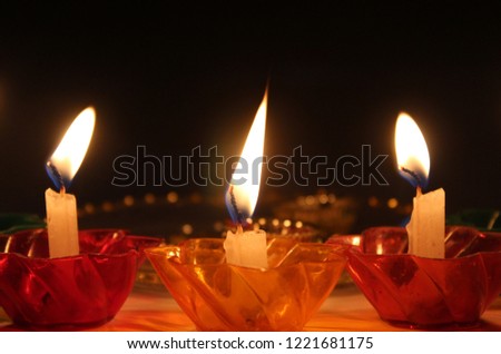 Group of burning candle-lights in coloured ( red, yellow and green) glass candle-holders, neutral background, Dark background, blurred, bokeh effect and light dots. No person. Space for text. festival
