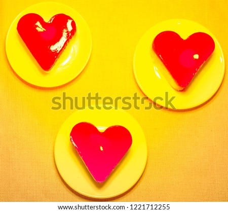 three red jelly heart-shaped cakes in circle plates on yellow background