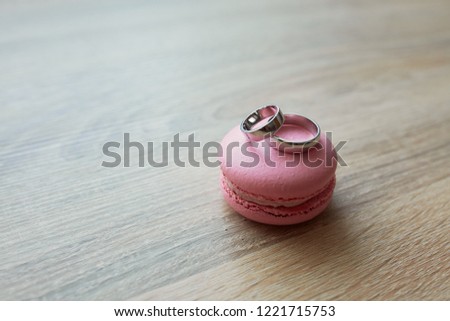 Golden wedding rings lie on a pink macaroon