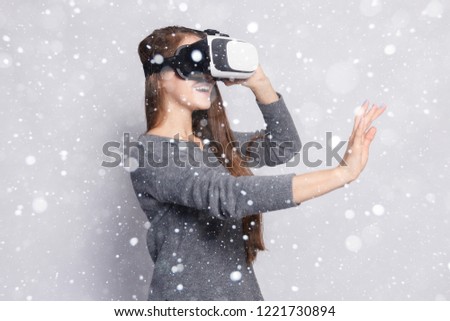snow, winter, christmas, technology, virtual reality, entertainment and people concept - happy woman virtual reality headset or 3d glasses. Woman with virtual reality goggles over snow background