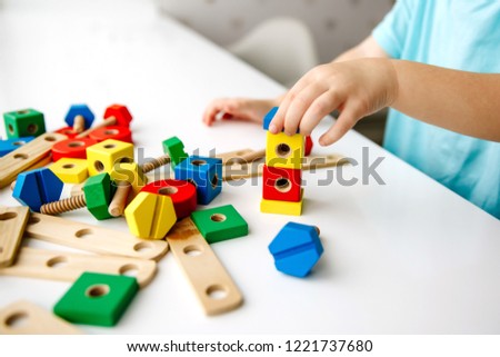 Close up of child hands playing with colorful wooden bricks at the table. Toddler having fun and building out of bright constructor bricks. Early learning