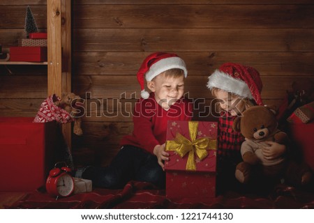Happy family in Christmas night. Children boy and girl opening presents in xmas interior. Kids looking to magic box with light from it. Kids in in red santa claus hats.