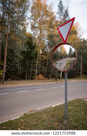 Road sign "give way" and outdoor convex protective mirror with a reflection of the urban road look car on a green background.