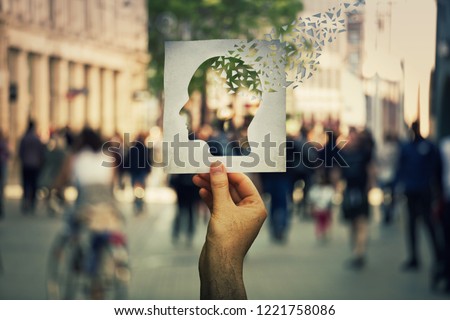 Hand holding a paper sheet with human head icon broken into pieces over a crowded street background. Concept of memory loss and dementia disease. Alzheimer's losing brain and memory function. Royalty-Free Stock Photo #1221758086