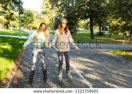 Two cheerful young girls on on roller skates spending time at the park, holding hands