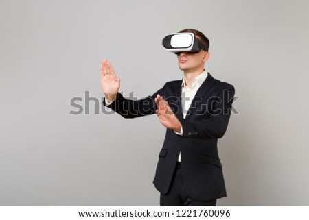 Young business man in suit looking in headset touch something like push click on button and pointing at floating virtual screen isolated on grey background. Achievement career wealth business concept