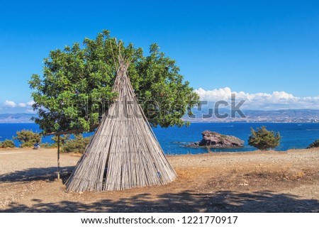 Picture of wooden wickiup like building with blue sky and clouds at the background.