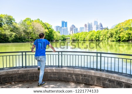 Young man standing in Piedmont Park in Atlanta, Georgia looking at scenic view, water, cityscape, skyline of urban city skyscrapers downtown, Lake Clara Meer
