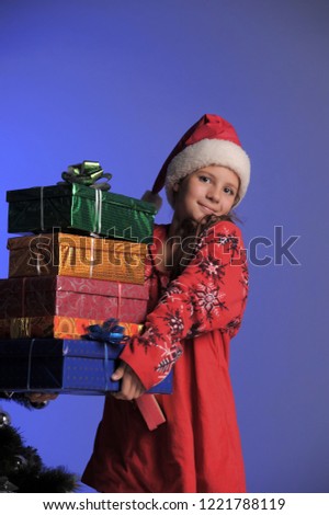 Cute smiling little girl with curly hairstyle wearing knitted sweater, scarf and hat holding christmas gift