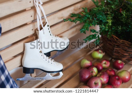Children skates on wooden bench in home interior in rustic style. Preparing for skating. Ripe apples near wicker basket with green branches. Christmas, winter, autumn mood.