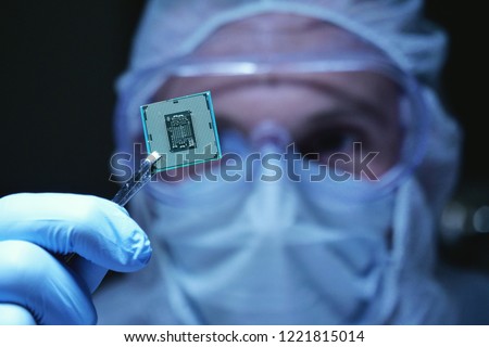 In Ultra Modern Electronic Manufacturing Factory Design Engineer in Sterile Coverall Holds Microchip with symbols in futuristic holography. artificial intelligence, future of robots.
 Royalty-Free Stock Photo #1221815014