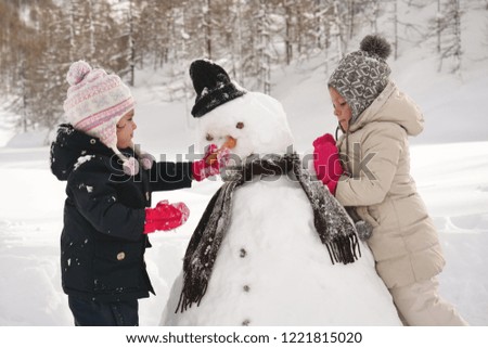 On a winter day, in the mountains with snow, two little girls play and play the snowman. Concept of: winter holidays, game, christmas, mountain
