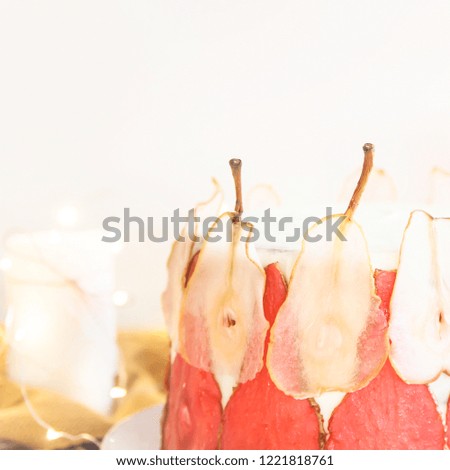 Festive white cake decorated with red and white pear slices On a white background among the gentle lights and candles