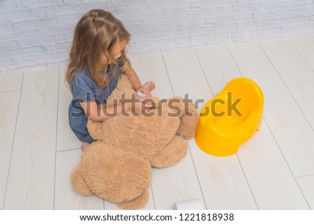 a against the background of a white brick wall, the girl sits on a potty with the child, wiping her ass with toilet paper