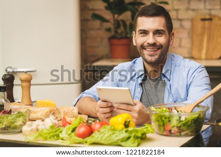 Man preparing delicious and healthy food in the home kitchen on a sunny day. Using tablet computer for searching recipes. 