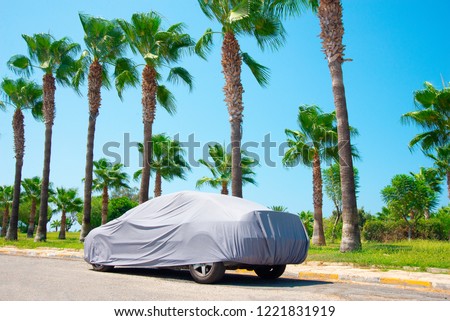 The car is in the parking with auto cover from the sun surrounded by palm trees. Hot countries, protection from heating the car. Royalty-Free Stock Photo #1221831919