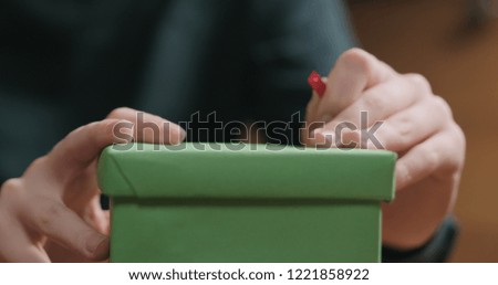 Closeup shot of female hands tying red ribbon bow on green paper gift box