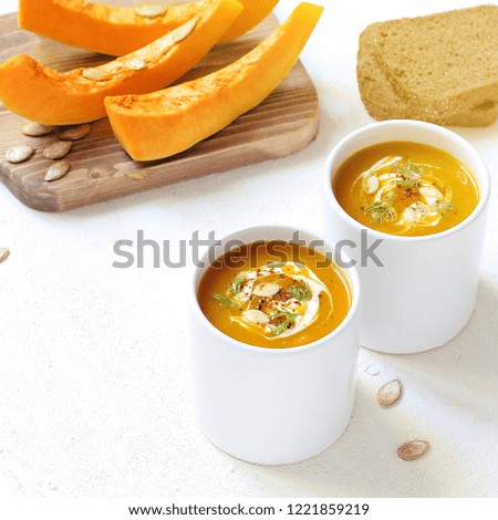 Roasted pumpkin and carrot soup with cream and pumpkin seeds on white background with butternut squash slices and green.Space for copy or text