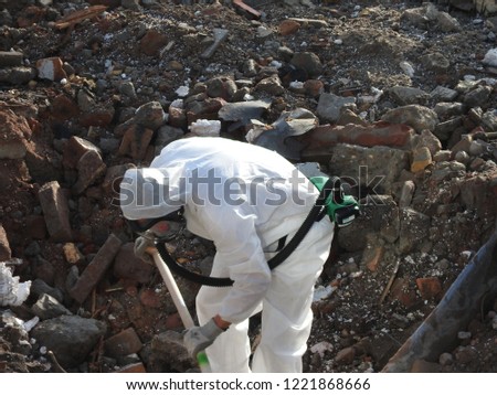 
Worker with special white suit, gloves and mask removes asbestos on construction site after demolition. Asbestos in background. Removal fiber cement containing asbest.Action picture, part of a serie.