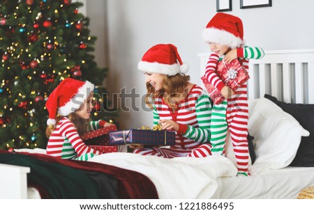 happy family mother and children  in pajamas  opening gifts on christmas morning near christmas tree
