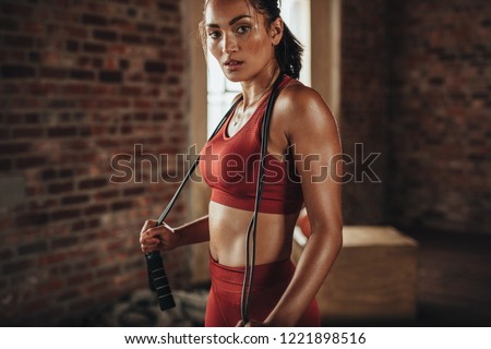 Fit and healthy woman standing at gym with skipping rope. Sportswoman resting after workout. Royalty-Free Stock Photo #1221898516