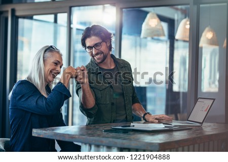 Young businessman and senior businesswoman making a fist bump at office. Business colleagues looking happy and excited after completion of project. Royalty-Free Stock Photo #1221904888