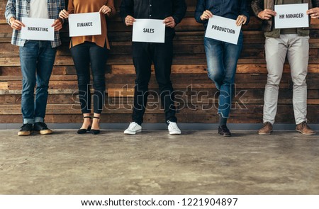 Low section of people standing against the wall holding names of their respective departments on a placard. Candidates shortlisted for different departments in an organization. Royalty-Free Stock Photo #1221904897