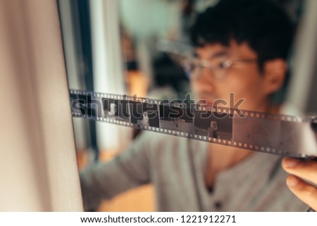 Man checking 35mm filmstrip in front of window. Photographer looking at a frames on old film. Focus on filmstrip.
