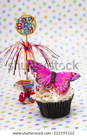 Close-up shot of cupcake with butterfly miniature and colorful happy birthday stand over polka dots surface.