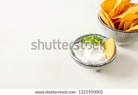 Snack for a party, chips with tortilla, nachos with sauces: salsa with tomatoes, sour cream. Mexican food. Bright white background.  Copy spaceю