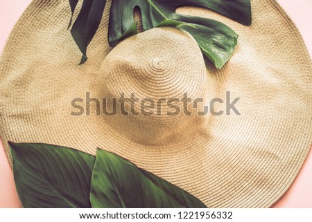 Stylish still life with a beach big hat and tropical leaves on a pink background