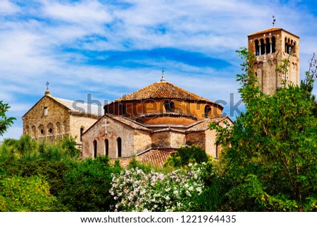 View of Torcello Cathedral, Church of Santa Fosca, bell tower, over green trees under blue sky, on the island of Torcello, Italy Royalty-Free Stock Photo #1221964435