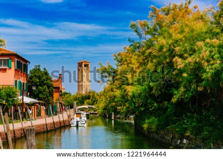 Canal with boats between houses and trees leading to the tower of Torcello Cathedral, under blue sky, on the island of Torcello, Venice, Italy Royalty-Free Stock Photo #1221964444