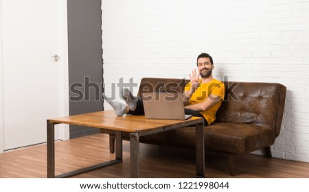 Man with his laptop in a room happy and counting four with fingers