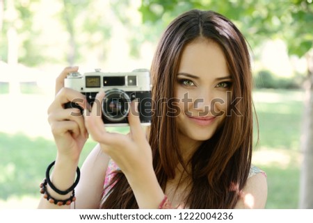 Cheerful beautiful girl talking pictures with vintage camera in summer park. Young woman photographer posing with her camera outdoor.