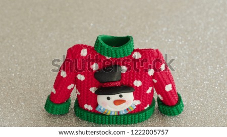 red sweater with green collar and sleeve cuffs white snowflakes and snowman with black hat and carrot nose on festive silver background with writing space