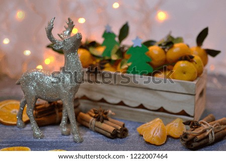 Christmas composition with statuette of deer, tangerines (oranges, Clementines, citrus fruits) with green leaves in box, cinnamon, star anise (warm light)