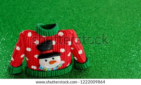 red sweater with green collar and sleeve cuffs white snowflakes and snowman with black hat and carrot nose isolated on a festive green background with writing space