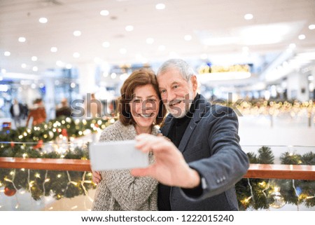 Senior couple with smartphone taking selfie in shopping center at Christmas time.