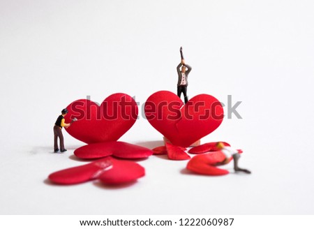 Miniature people breaking red hearts