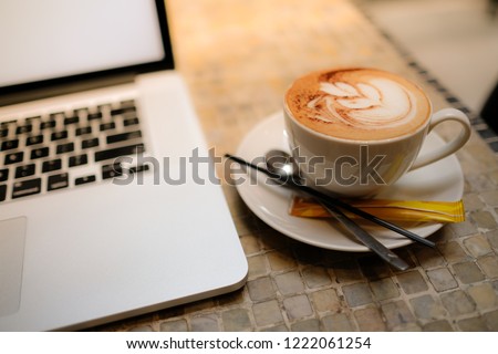 A cup of cappuccino coffee or latte coffe in a white cup with laptop on table. Royalty high quality free stock photo of drink capuccino or latte coffe with laptop for working in office