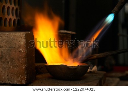 Silver pellets being melted in a red hot melting pot with a blowtorch, producing beautiful orange flames