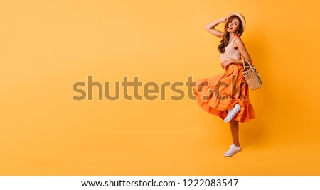 Magnificent woman in long bright skirt dancing in studio. Carefree inspired female model posing with pleasure on yellow background.