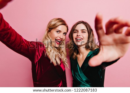Good-humoured lady in red outfit fooling around with best friend. Glamorous caucasian girls preparing for party.