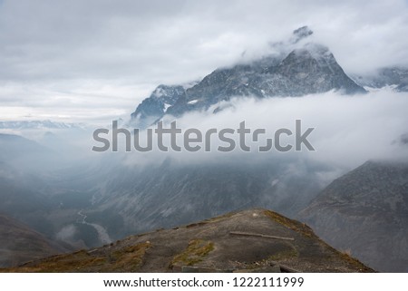 Mountain ranges partly engulfed in clouds with river leading into the picture, Tour de Mont Blanc