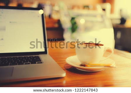 A cup of cappuccino coffee or latte coffe in a white cup with laptop on table. Royalty high quality free stock photo of drink capuccino or latte coffe with laptop for working in coffee shop 