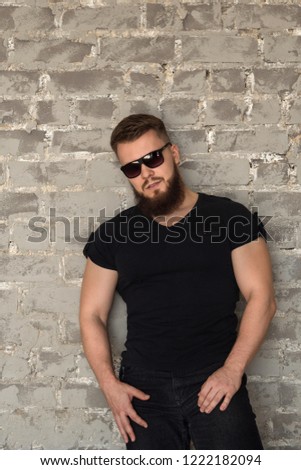 Bodybuilder in sunglasses portrait. Muscular man with a beard in the tight-fitting T-shirt standing at the brick wall. Stylish and sporty young man.
