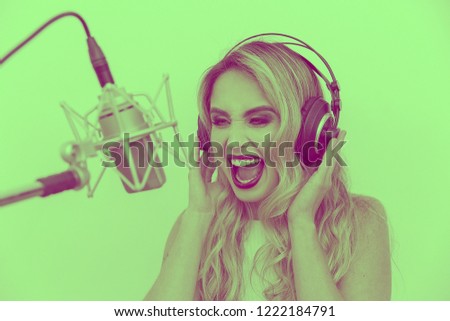 Portrait of a young woman singer with headphones in front of the microphone. Sing with an expression of happiness