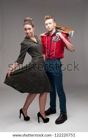 cheerful young caucasian guitar player and dancing girl in vintage clothing over gray background