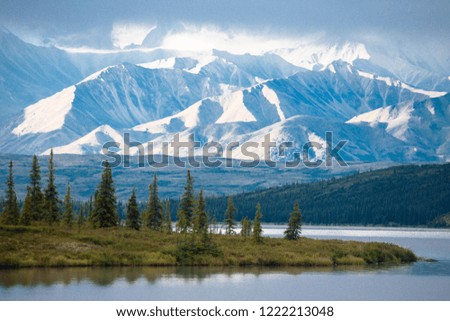 Breathtaking view of snow capped mountain top with blue sky and trees in Alaska